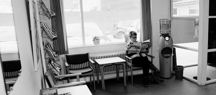 Ældre kvinde læser avis og venter på fysioterapeutisk behandling.